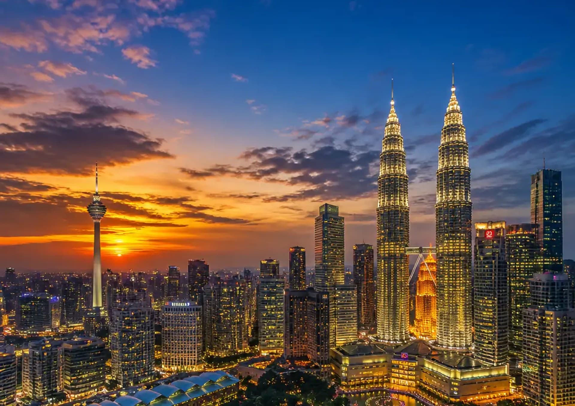 The Kuala Lumpur skyline at dusk, the Petronas Twin Towers and KL Tower lit against the sunset